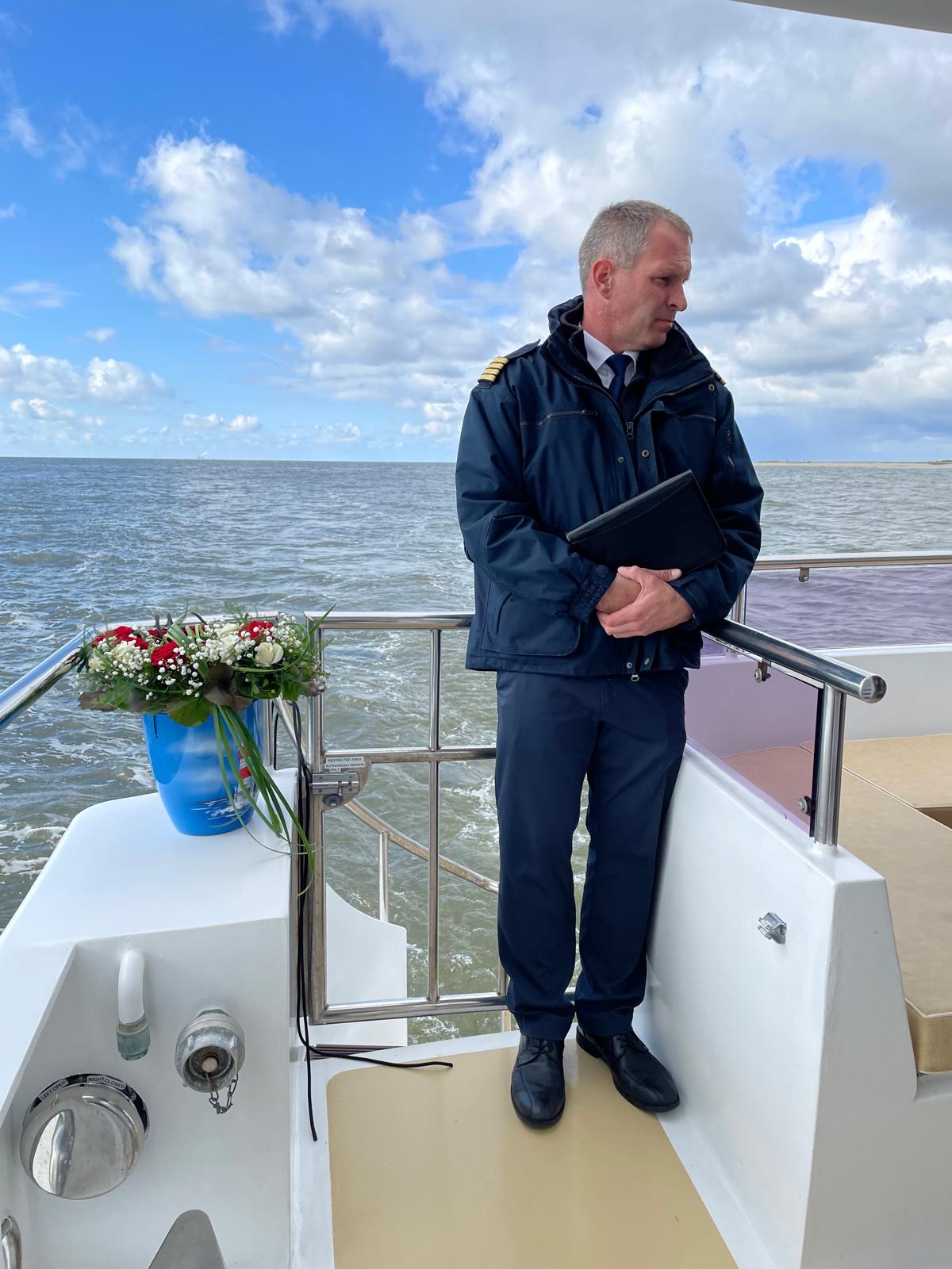 Mann steht mit einer dekorierten Urne auf einem Boot